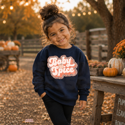 Toddler girl wearing a navy "Baby Spice" sweatshirt with a retro pumpkin graphic surrounded by pumpkins and fall decorations.