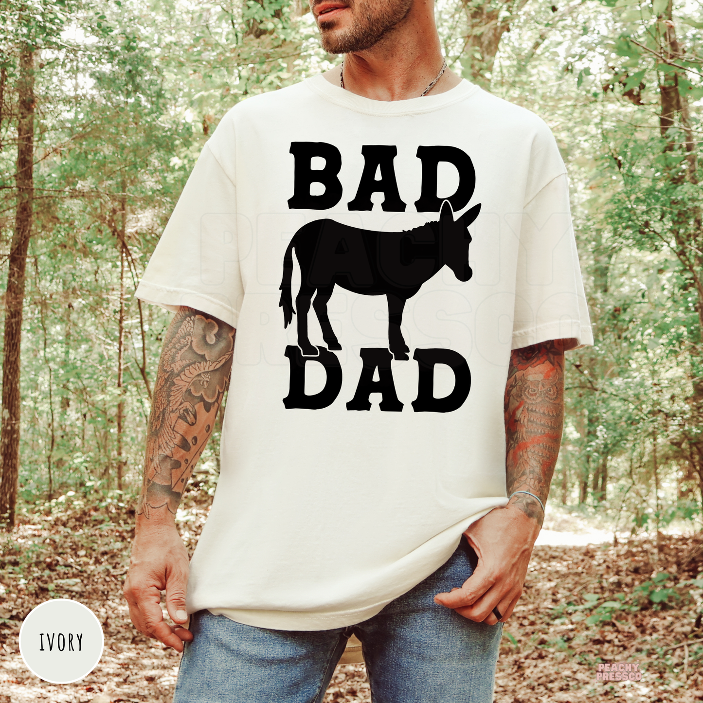 Ivory unisex t-shirt featuring a black donkey silhouette with "Bad Ass Dad" western-inspired graphic for funny dad gifts.