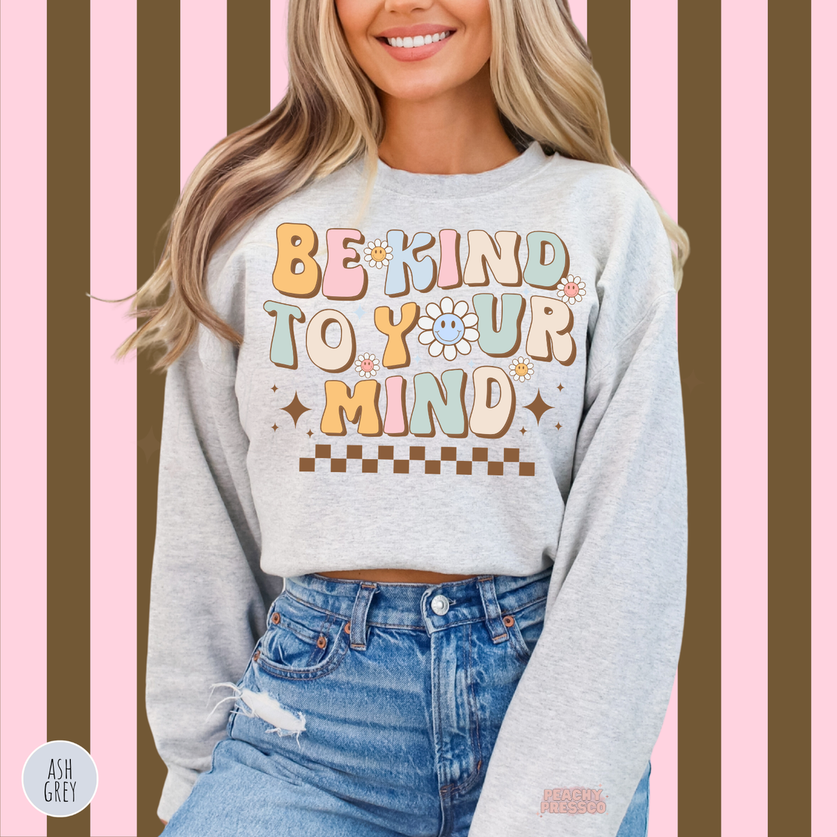 Ash grey Be Kind to Your Mind sweatshirt featuring pastel pink, blue, yellow and sage green lettering with smiling daisies and a retro checkerboard accent.