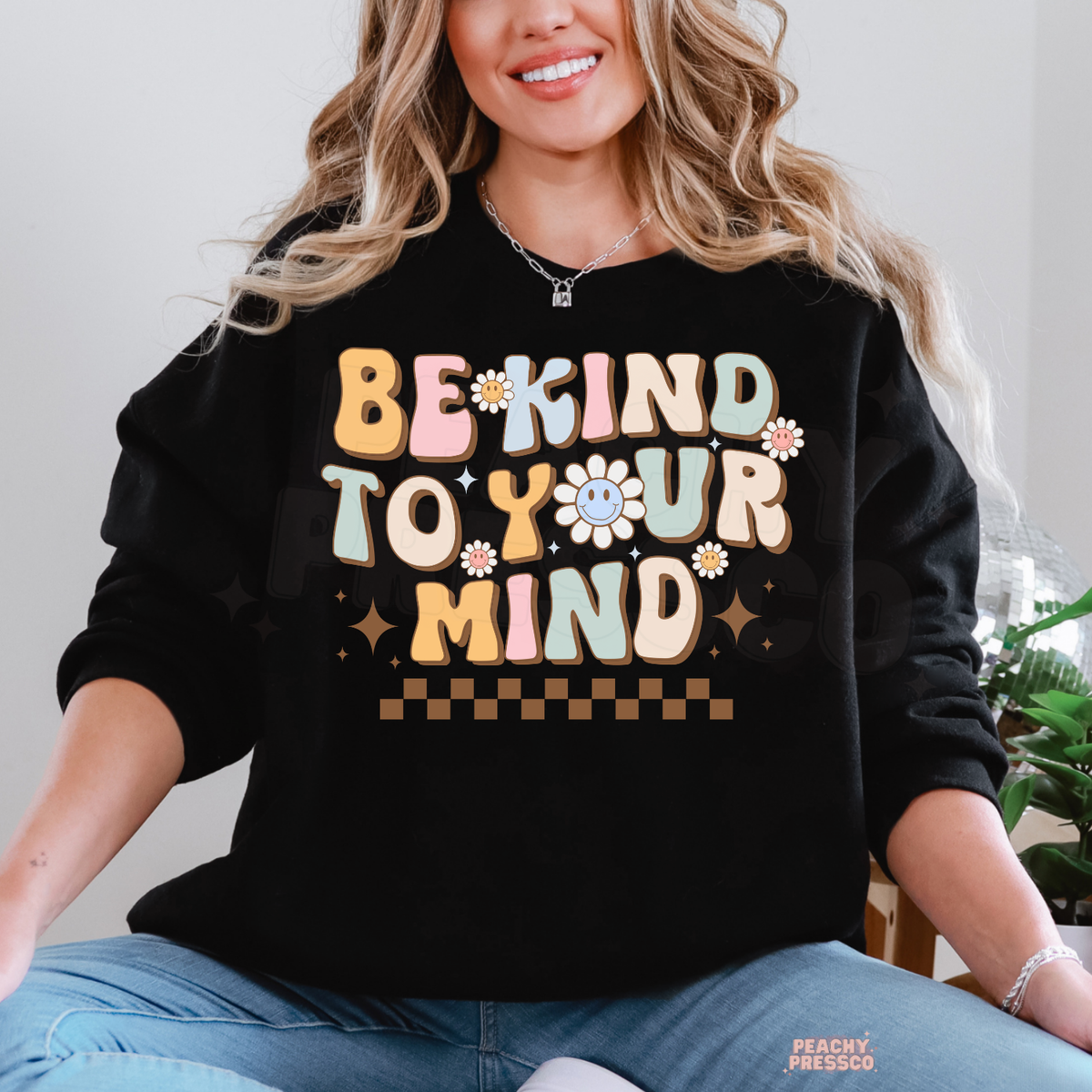 Black Be Kind to Your Mind sweatshirt featuring pastel retro lettering, smiling daisy flowers, brown sparkles and a cheerful mental health awareness design.