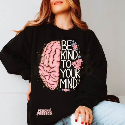 Black sweatshirt featuring a vibrant pink brain illustration, floral details, and the inspirational phrase "Be Kind to Your Mind" in bold modern typography.