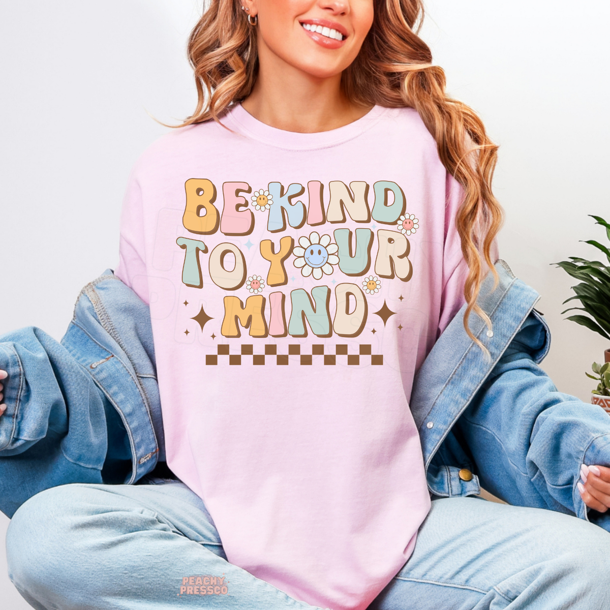 Light pink Be Kind to Your Mind shirt featuring colourful groovy lettering, cute smiling flowers, retro sparkles and a cheerful self-love affirmation.