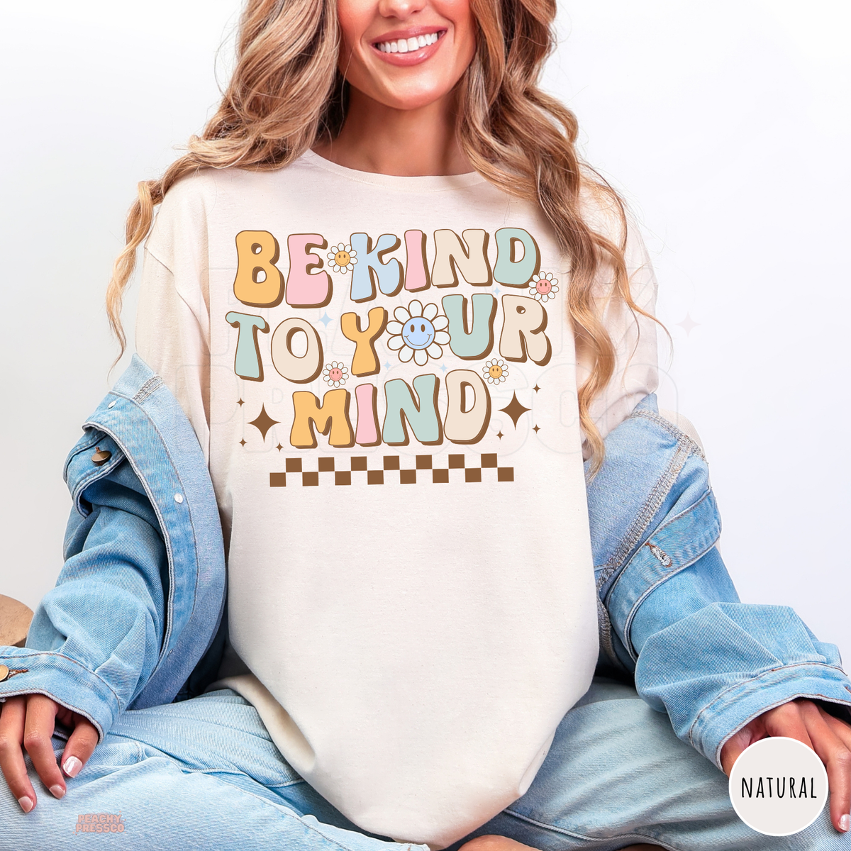 Natural Be Kind to Your Mind shirt featuring pastel retro bubble letters, smiling daisies, brown sparkles and a checkerboard design promoting self-love.