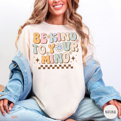 Natural Be Kind to Your Mind shirt featuring pastel retro bubble letters, smiling daisies, brown sparkles and a checkerboard design promoting self-love.