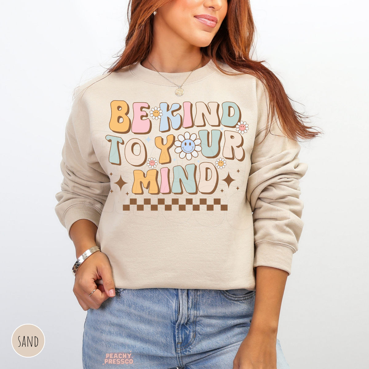Sand Be Kind to Your Mind sweatshirt with retro pastel typography, happy daisy illustrations, brown stars and a positive mental wellness message.