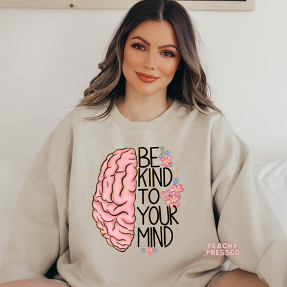 Sand sweatshirt with a pink brain graphic, delicate flowers, and the motivational quote "Be Kind to Your Mind" promoting mental health awareness and self-care.