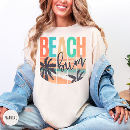 Woman wearing a natural colored tshirt featuring a retro "Beach Bum" beach design with palm trees, ocean sunset, and vintage-inspired tropical artwork.