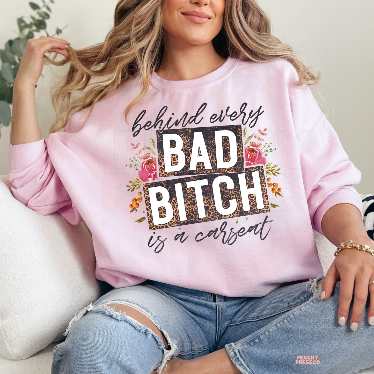 Woman wearing a light pink sweatshirt featuring behind every bad bitch is a carseat floral leopard print mom graphic.