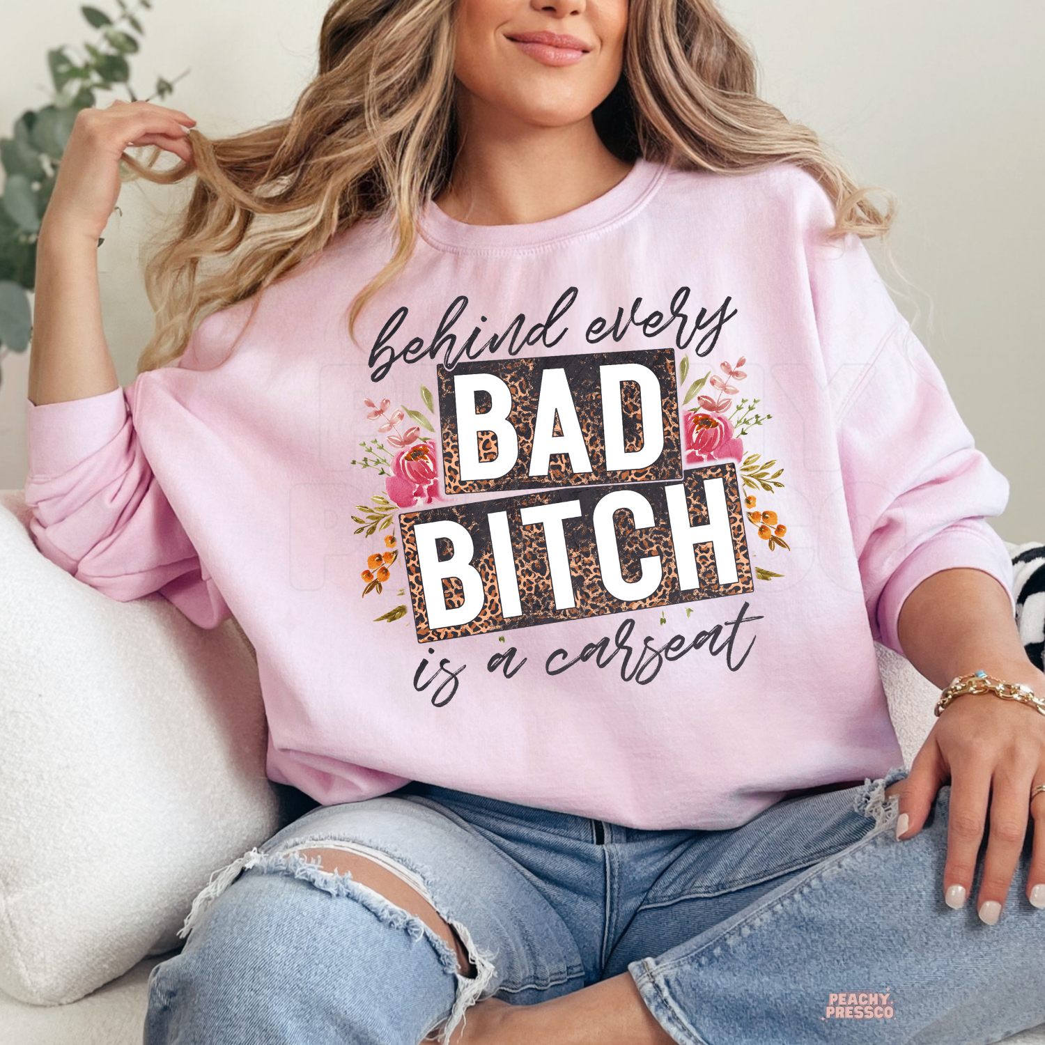 Woman wearing a light pink sweatshirt featuring behind every bad bitch is a carseat floral leopard print mom graphic.