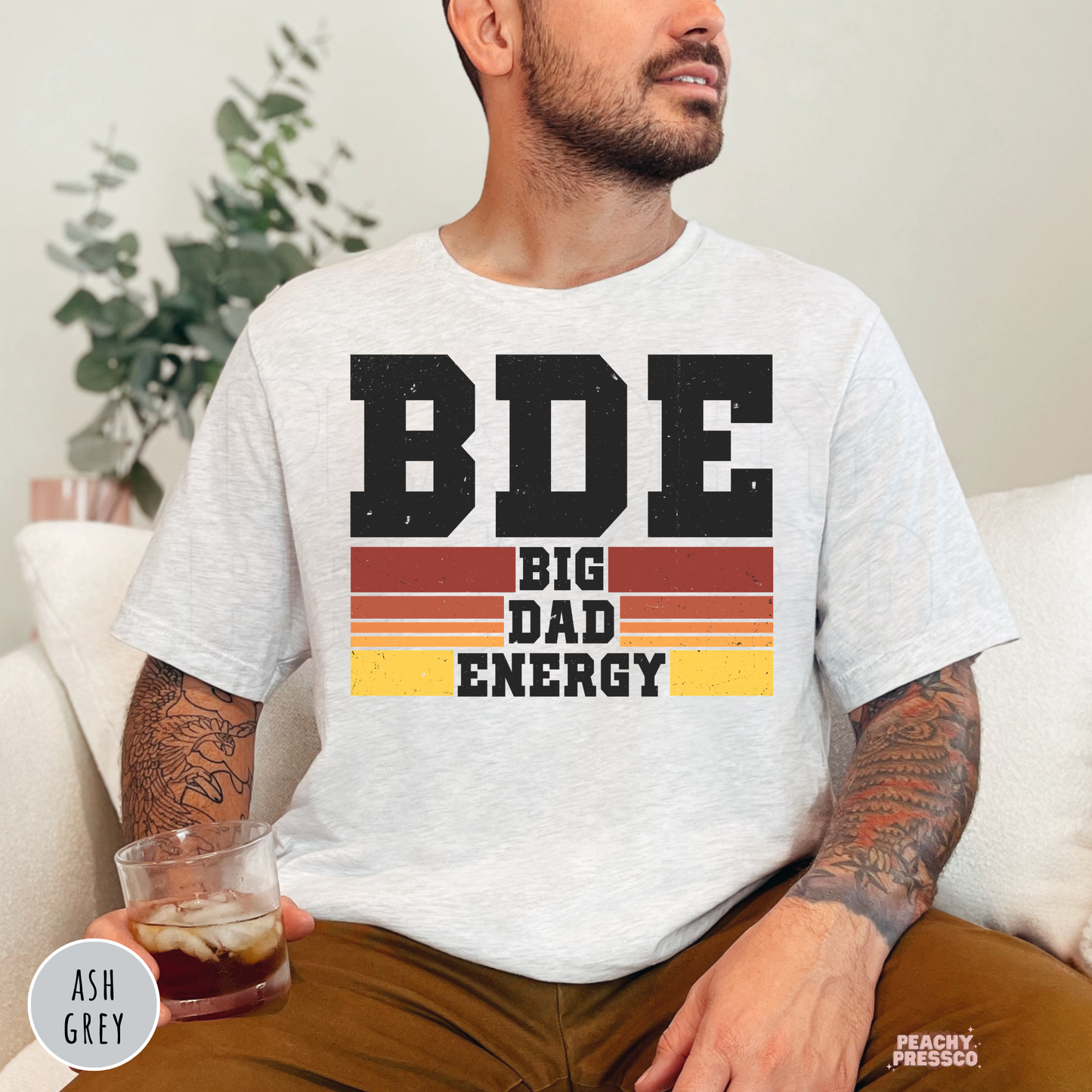 Ash Grey unisex t-shirt featuring the Big Dad Energy design with distressed black lettering and vintage sunset stripes, a funny Father's Day shirt for dads.
