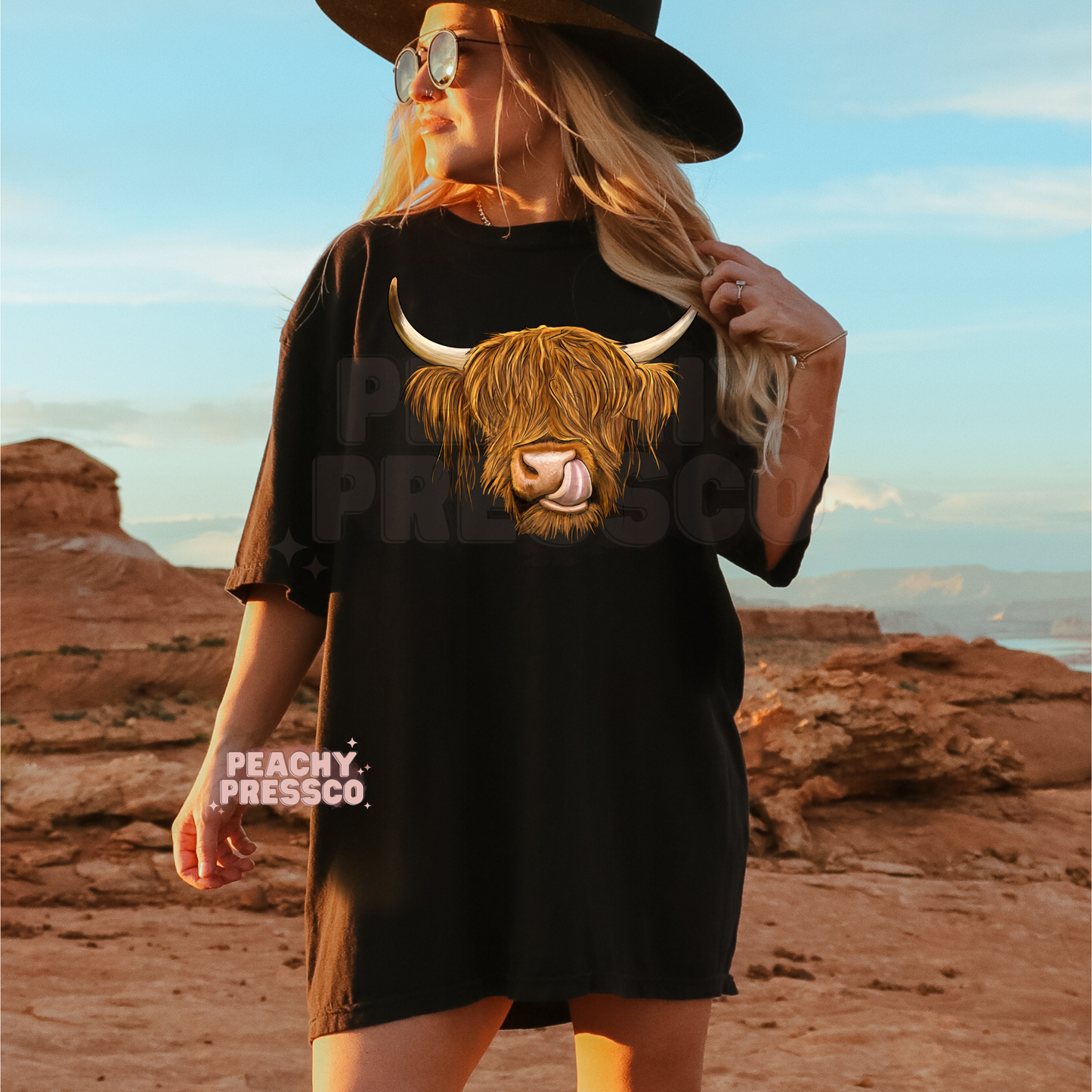 Woman wearing a black oversized t-shirt featuring a Highland cow graphic in a western desert landscape.