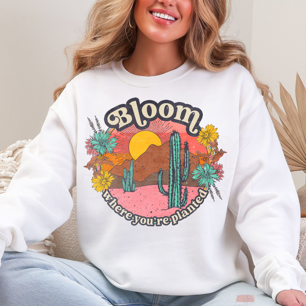 White Bloom Where You're Planted sweatshirt featuring a vintage-inspired desert landscape with colorful wildflowers, sunset, mountains, and green cacti.