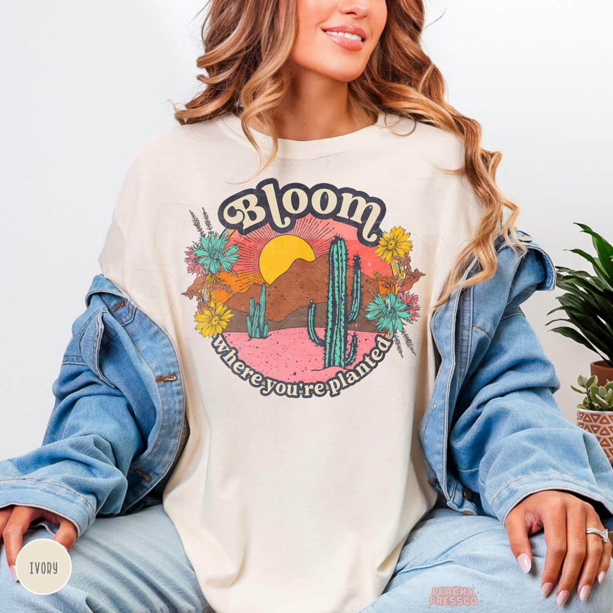 Ivory Bloom Where You're Planted graphic shirt featuring a vibrant desert sunset, turquoise cacti, yellow wildflowers, and positive botanical message.
