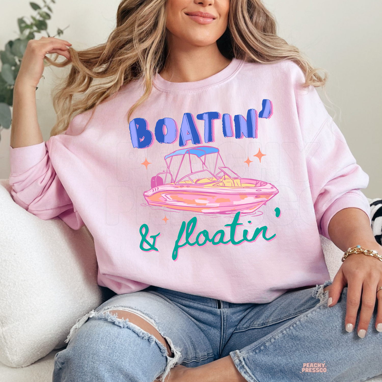 Light pink crewneck sweatshirt featuring a vibrant retro "Boatin' & Floatin'" graphic with a pink pontoon boat, bold blue lettering, and teal script—perfect for lake days, boating trips, and summer weekends.
