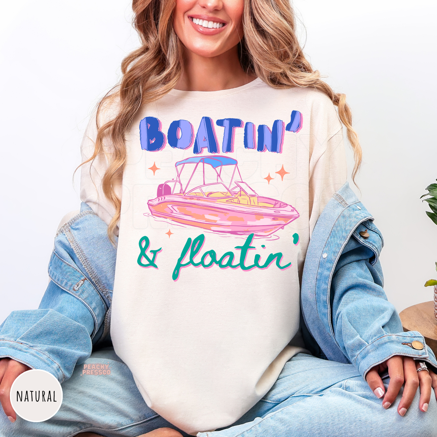 Natural shirt featuring a colorful "Boatin' & Floatin'" graphic with a retro pink pontoon boat, perfect for lake lovers and boating weekends.