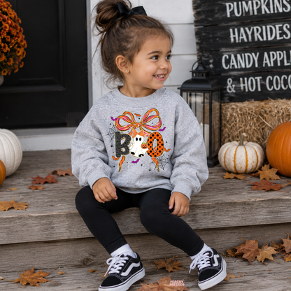 Girl wearing a sport grey Halloween sweatshirt featuring a cute BOO ghost and colorful bow graphic with pumpkins in the background.