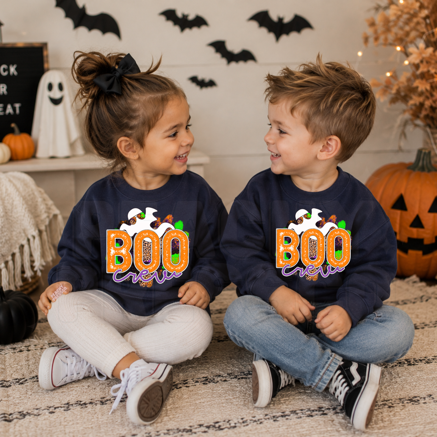 Toddler boy and girl wearing matching navy Boo Crew Halloween sweatshirts with a colorful ghost graphic in a cute Halloween setting.