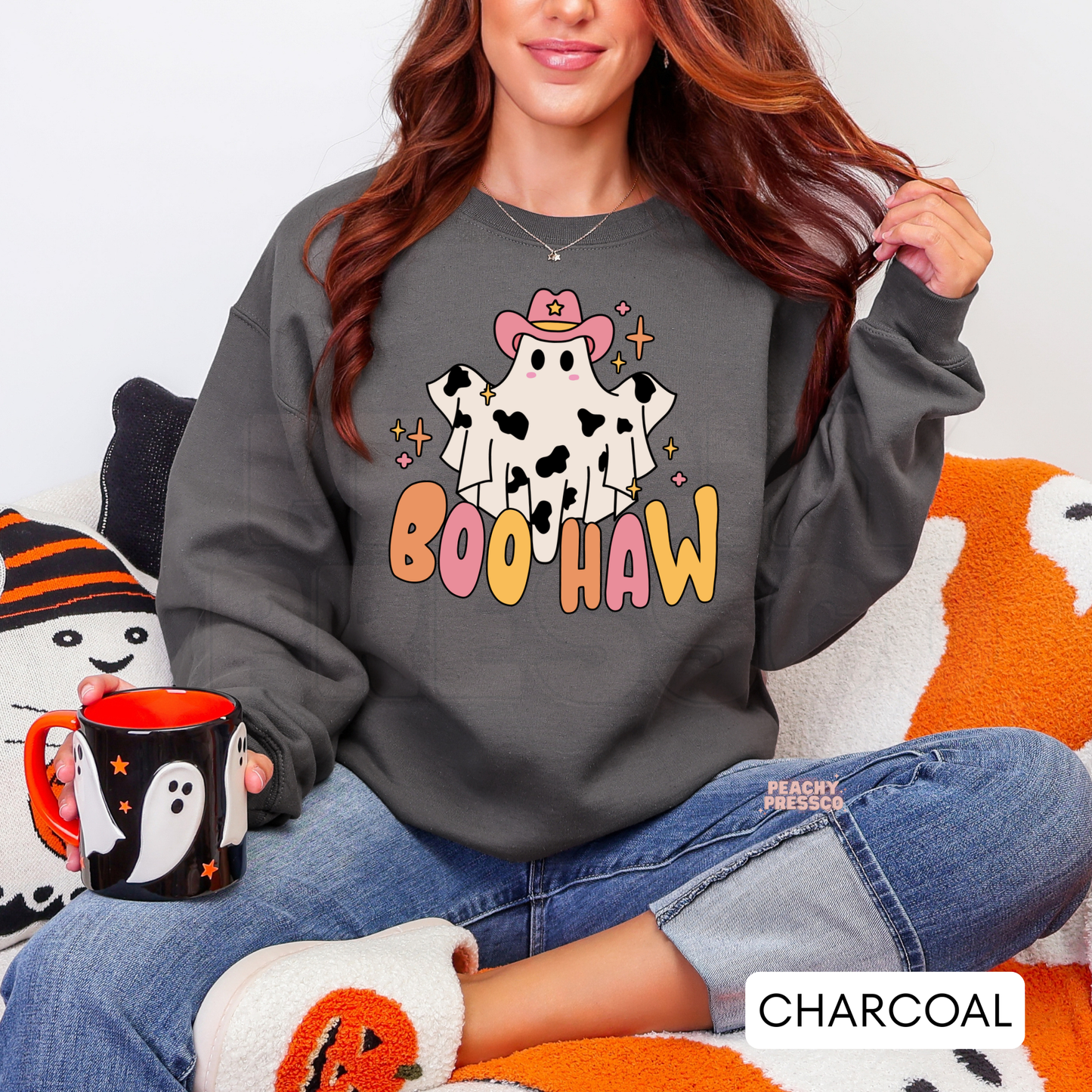 Woman wearing a charcoal Halloween crewneck sweatshirt with a cute cowgirl ghost Boo Haw graphic while holding a ghost mug.