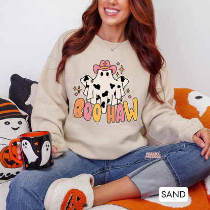 Woman wearing a sand crewneck sweatshirt with a cute cowgirl ghost Boo Haw Halloween design and cozy fall décor.