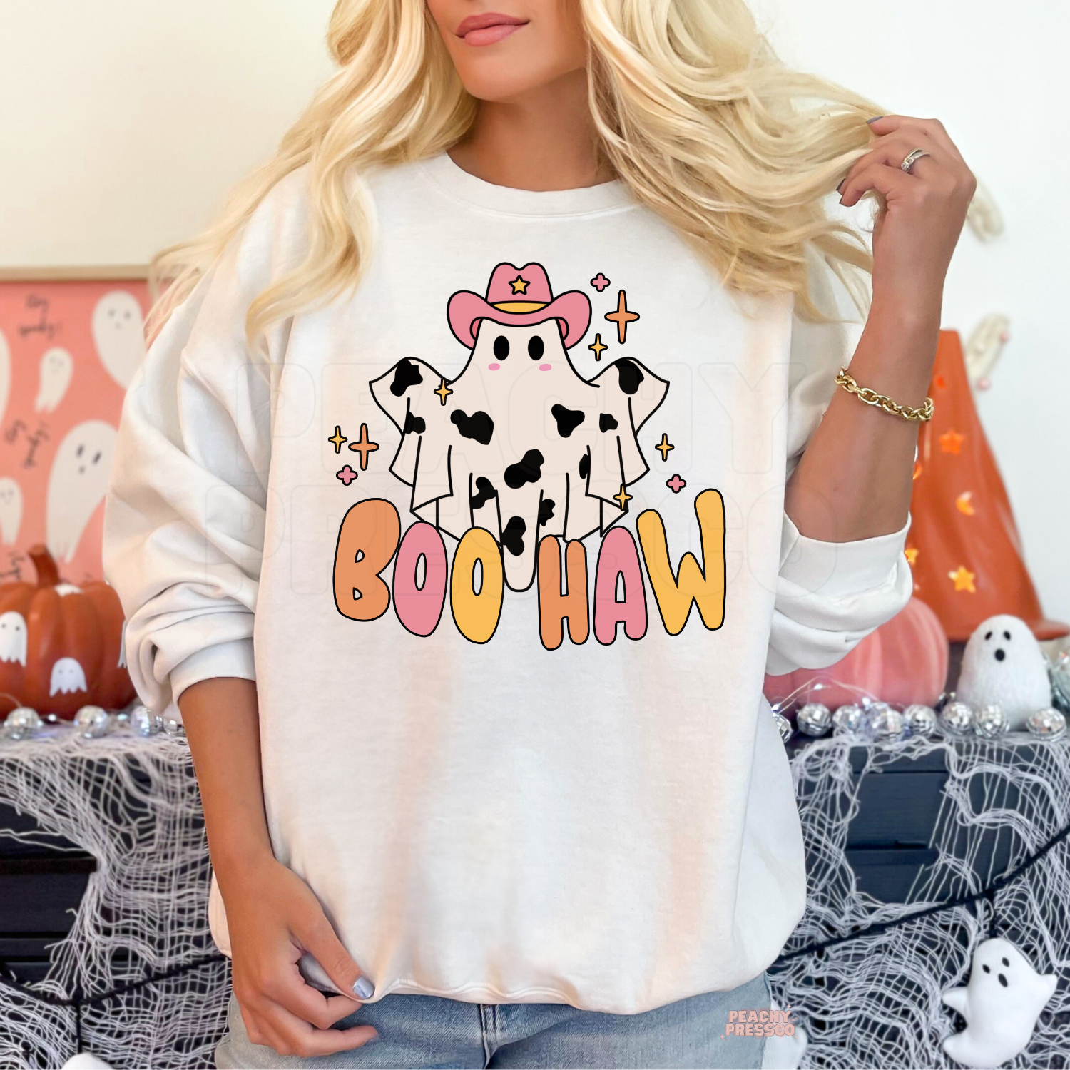 Woman wearing a white crewneck sweatshirt featuring a cute cowgirl ghost with pink cowboy hat and Boo Haw Halloween graphic.