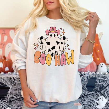 Woman wearing a white crewneck sweatshirt featuring a cute cowgirl ghost with pink cowboy hat and Boo Haw Halloween graphic.