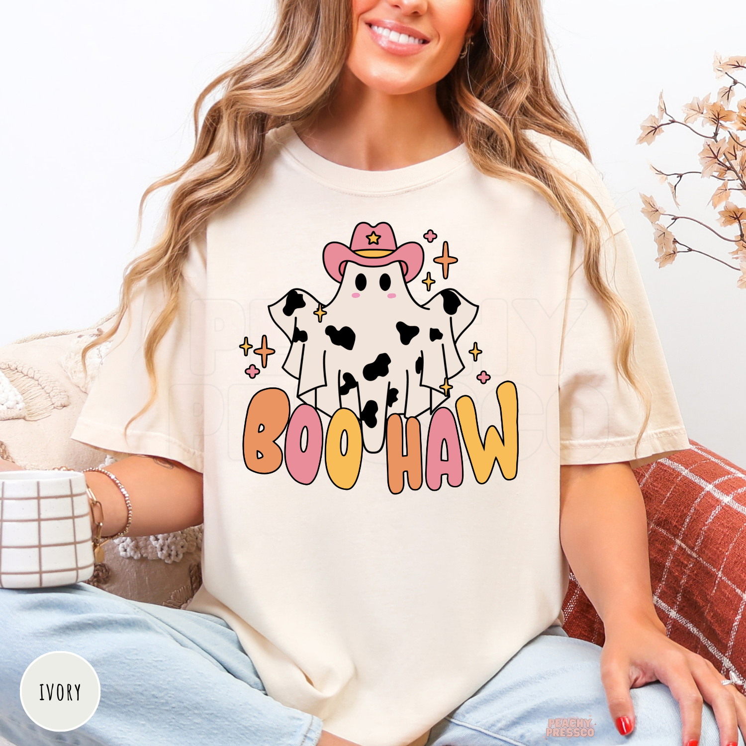 Woman wearing an ivory Comfort Colors Boo Haw Halloween graphic t-shirt with a pink cowgirl ghost design.