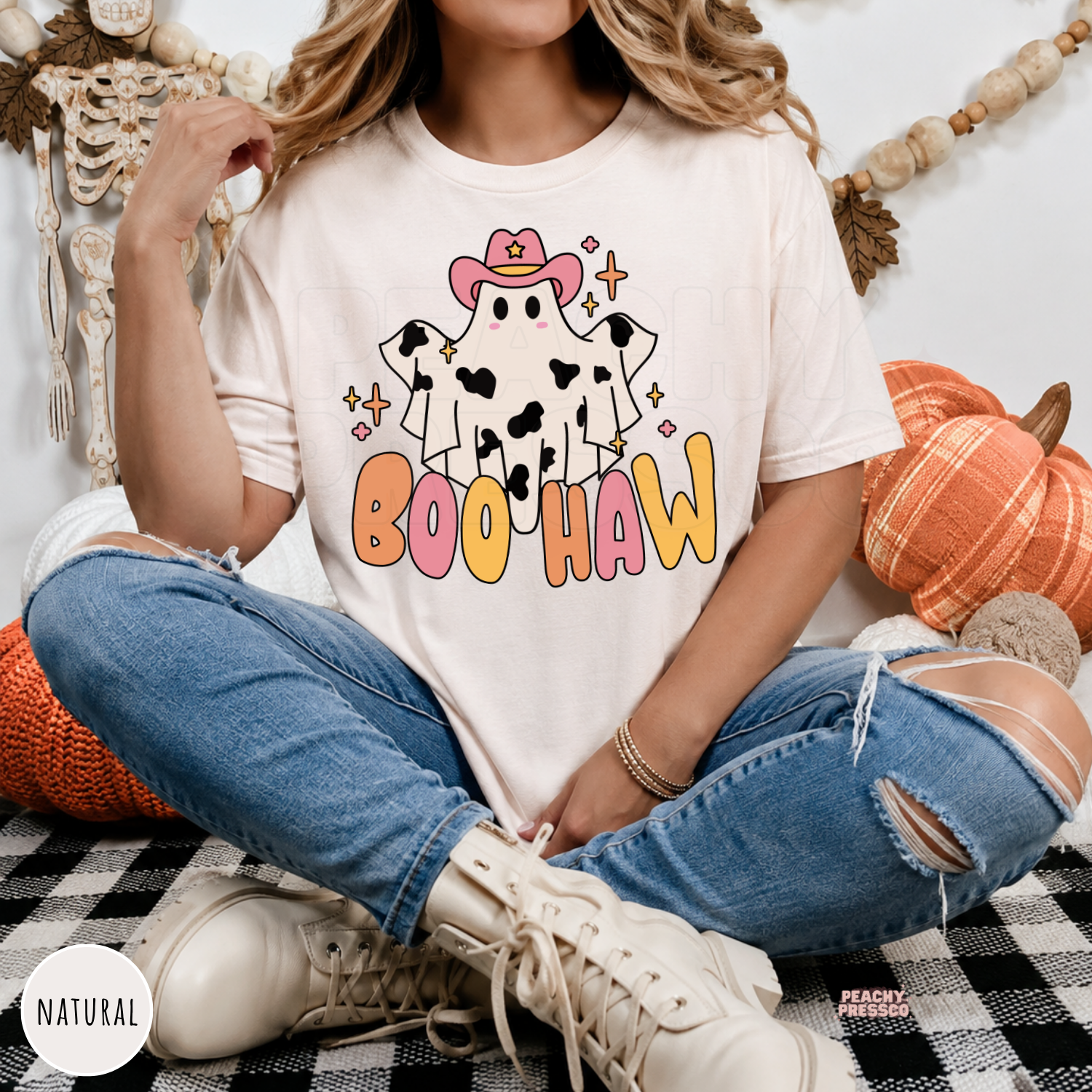 Woman wearing a natural colored Boo Haw Halloween graphic t-shirt with a cute western ghost and colorful lettering.