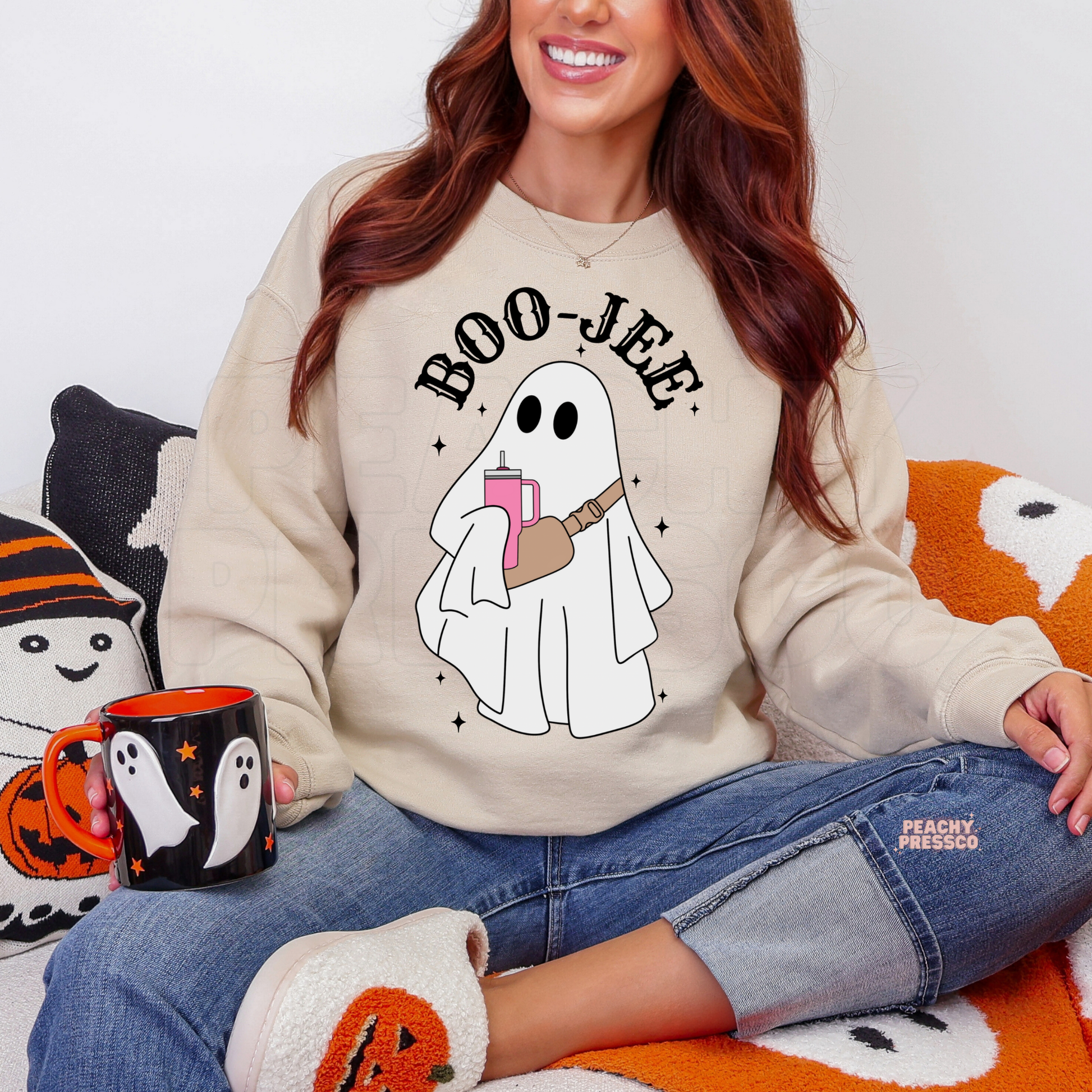 Woman wearing a sand Boo-Jee ghost crewneck sweatshirt with Halloween ghost graphic in cozy fall setting.