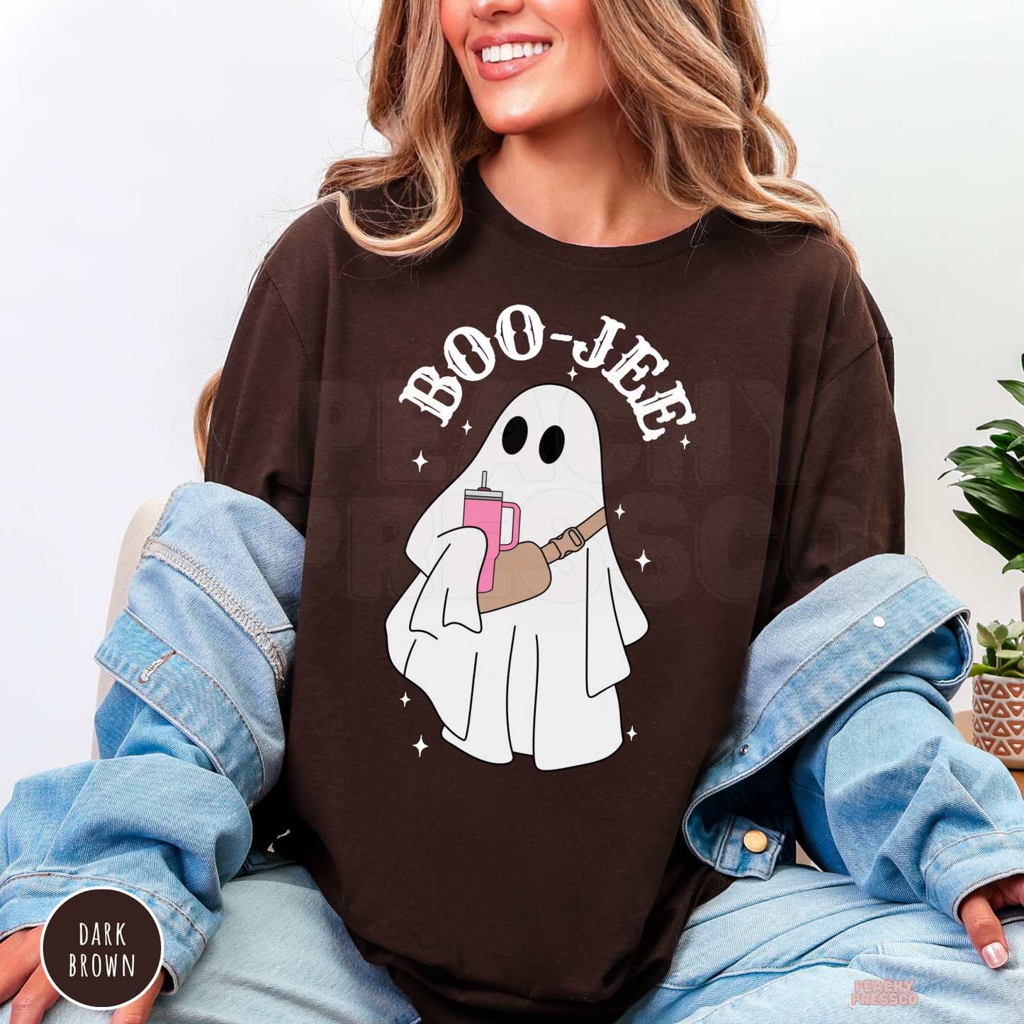 Woman wearing a dark brown Boo-Jee ghost Halloween shirt with trendy ghost graphic holding a pink tumbler.
