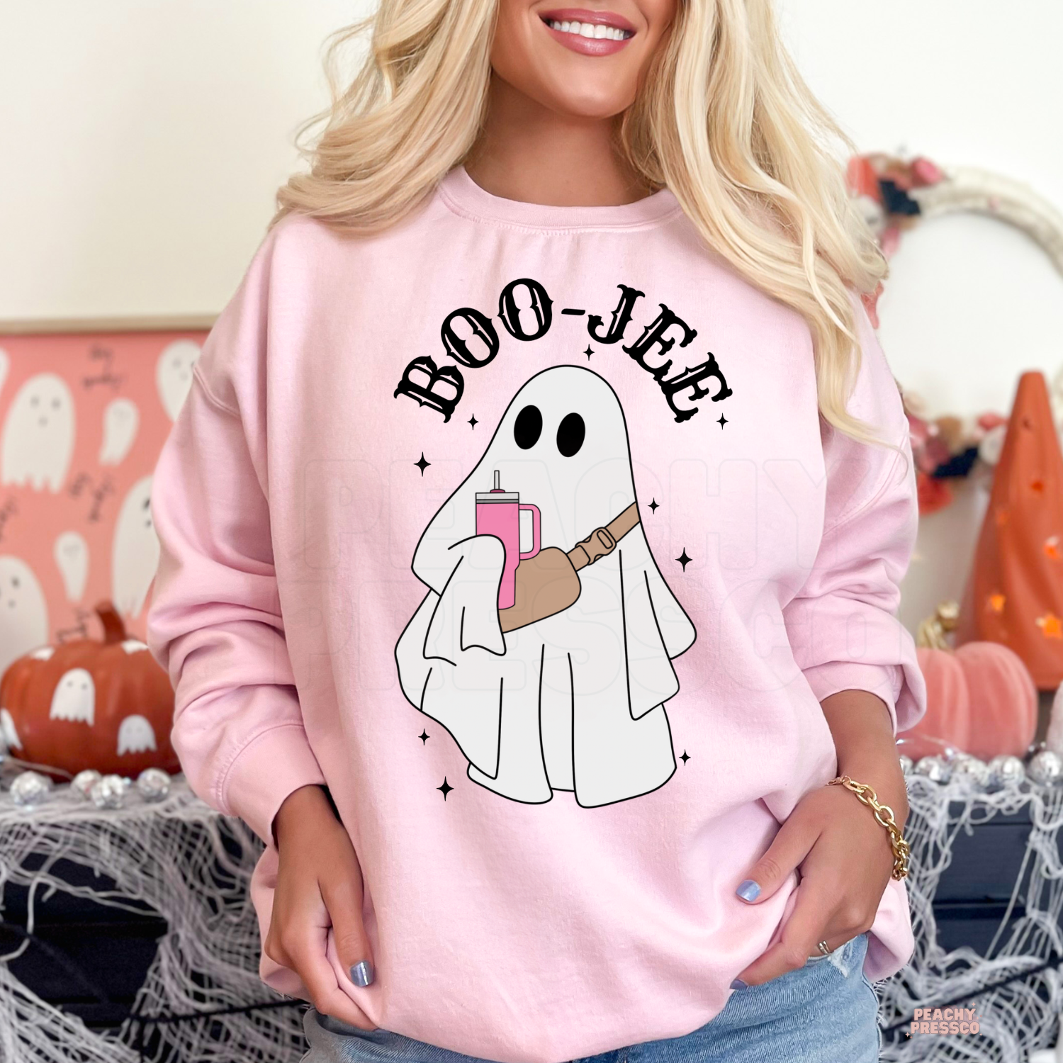 Woman wearing a light pink Boo-Jee ghost Halloween crewneck sweatshirt with cute ghost holding a tumbler.