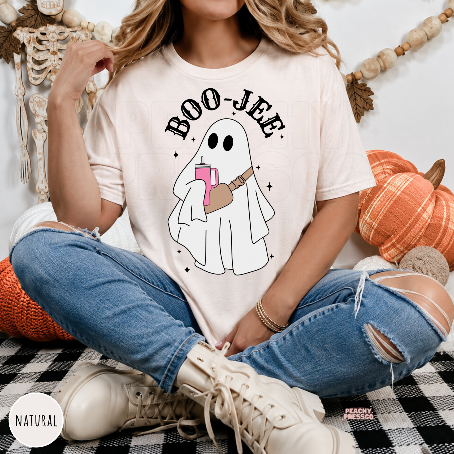 Woman wearing a natural colored Boo-Jee ghost Halloween t-shirt with cute ghost graphic in cozy autumn setting.