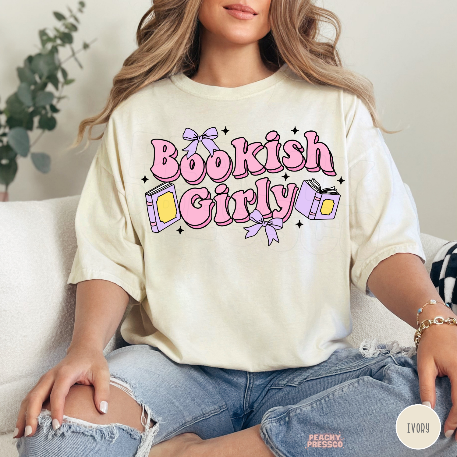 Woman wearing an ivory Comfort Colors t-shirt with a pastel "Bookish Girly" design featuring pink lettering, books, lavender bows, and sparkles. Relaxed oversized book lover aesthetic.