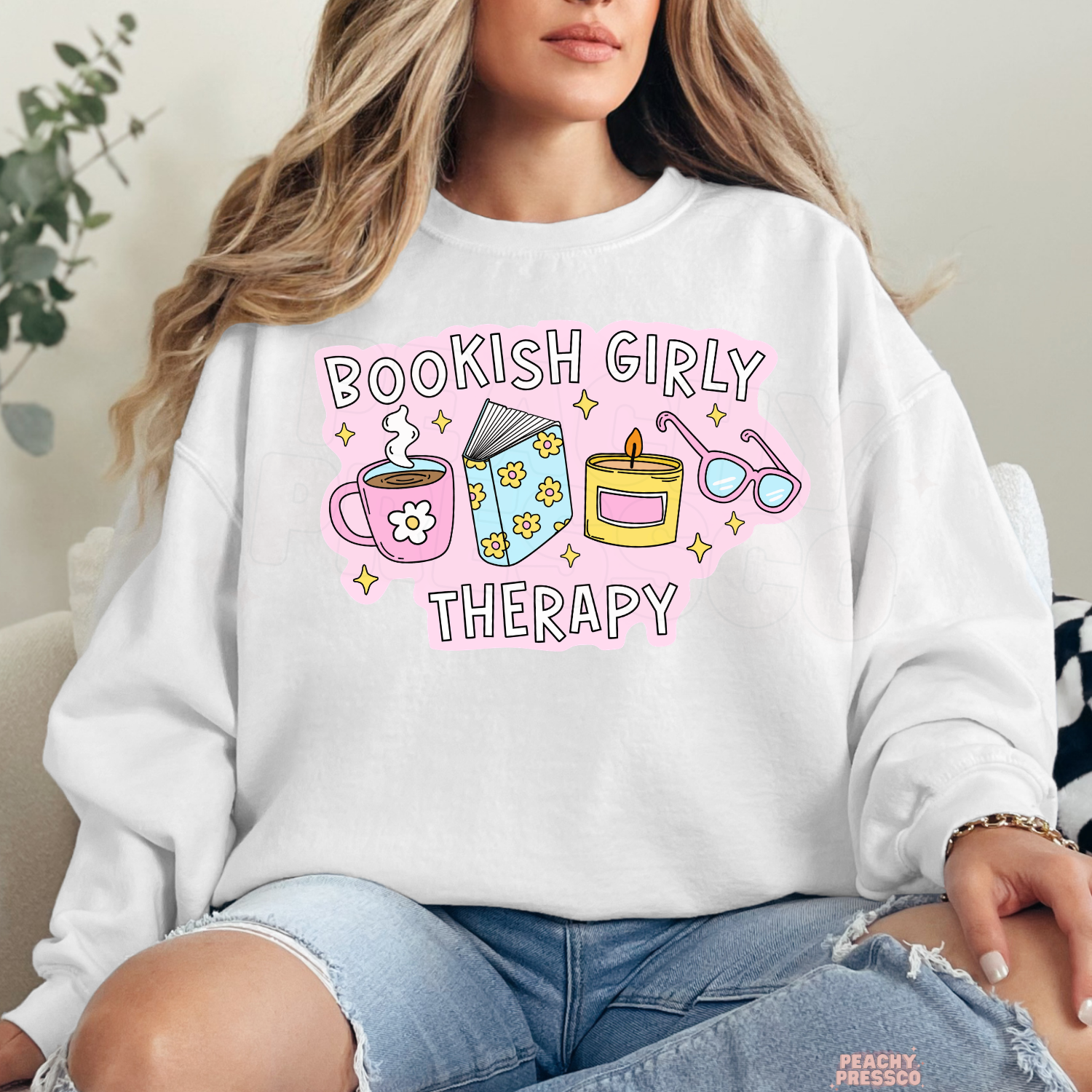 White crewneck sweatshirt featuring the Bookish Girly Therapy graphic with cozy reading-themed illustrations.