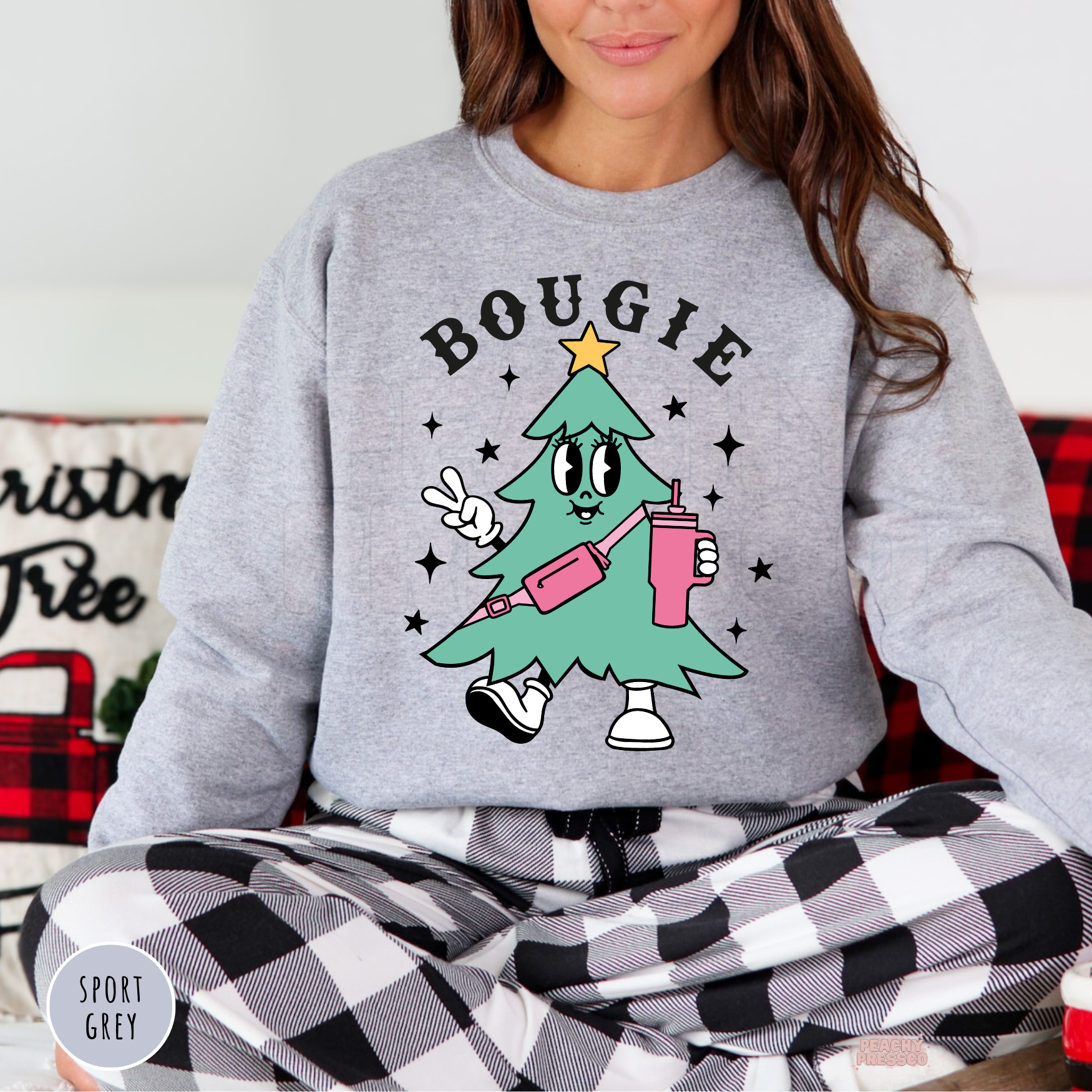 Woman sitting cross-legged in black and white plaid pajama pants wearing a sport grey Bougie Christmas tree graphic crewneck.