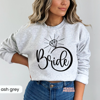 Ash grey crewneck sweatshirt with a modern black "Bride" engagement ring graphic, ideal for brides-to-be, bridal weekends, and honeymoon travel.