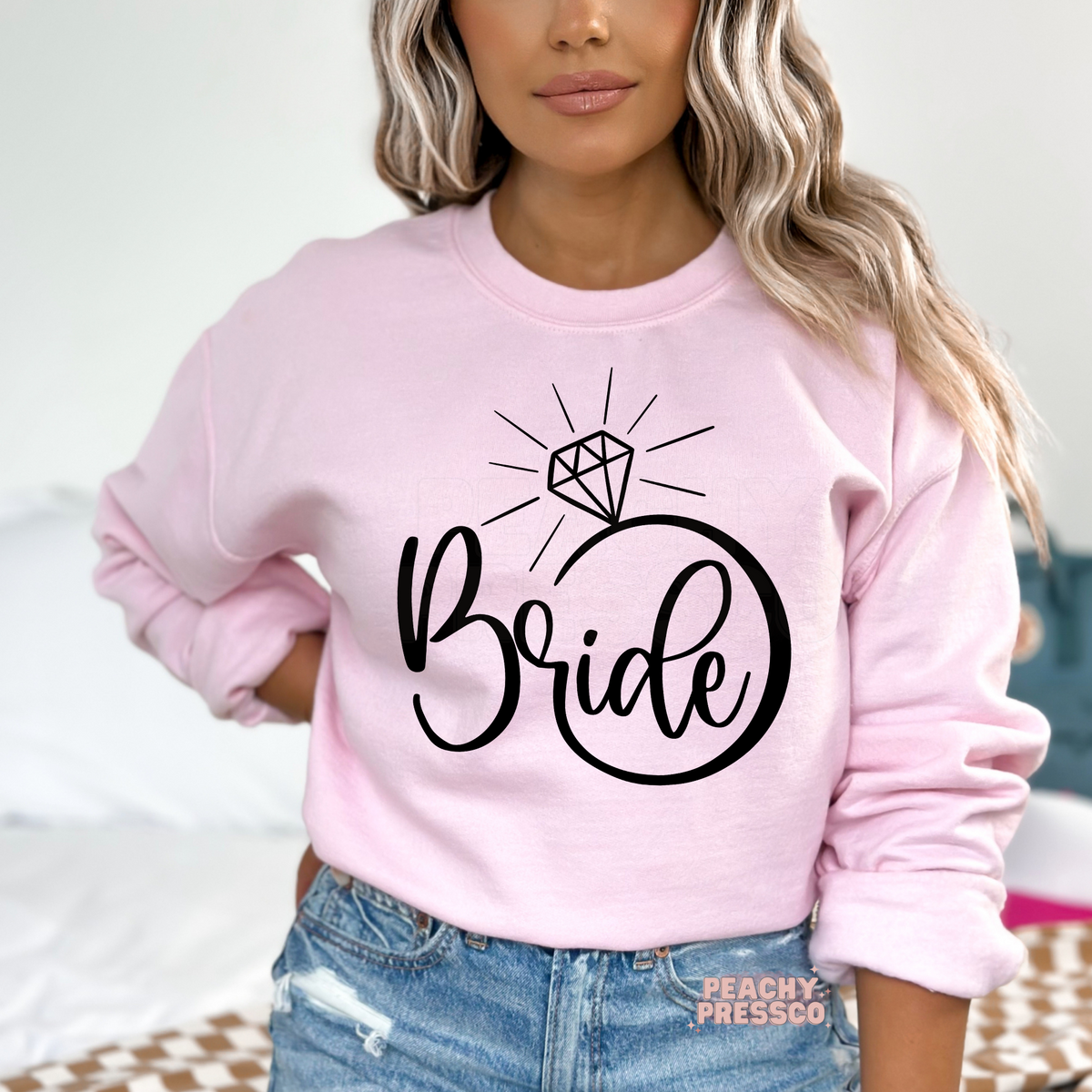 Light pink sweatshirt featuring a modern black "Bride" engagement ring graphic, a stylish choice for bachelorette weekends, bridal gifts, and wedding celebrations.