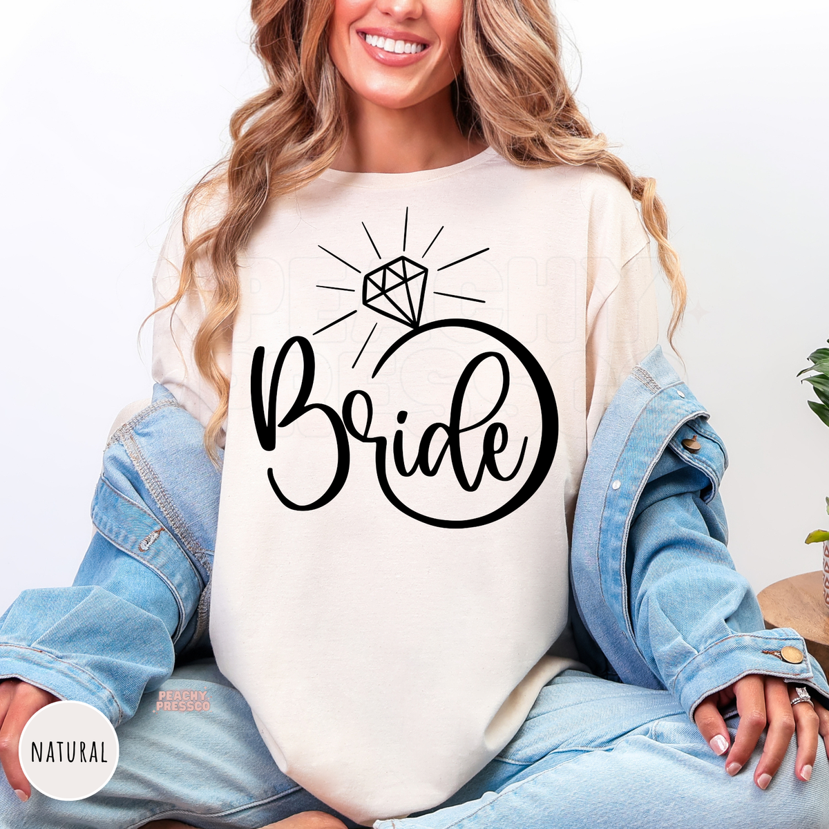 Natural t-shirt featuring a simple black "Bride" ring design with a diamond accent, perfect for engagement photos, bridal events, and wedding festivities.