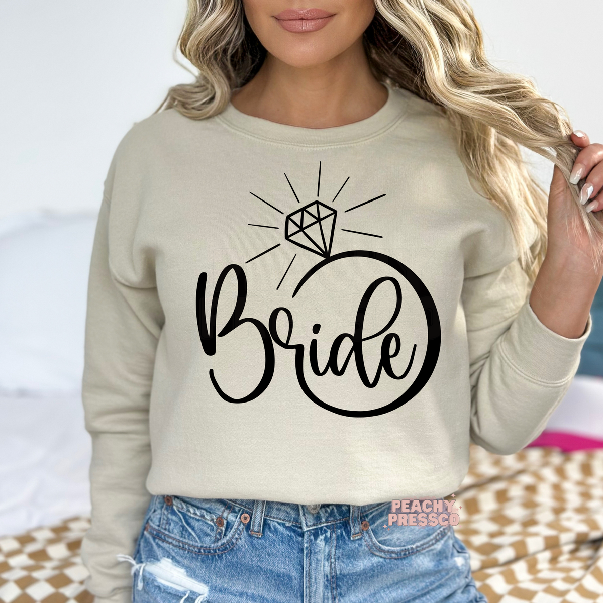 Sand crewneck sweatshirt displaying a clean black "Bride" diamond ring graphic, ideal for brides, bridal party events, and cozy honeymoon apparel.