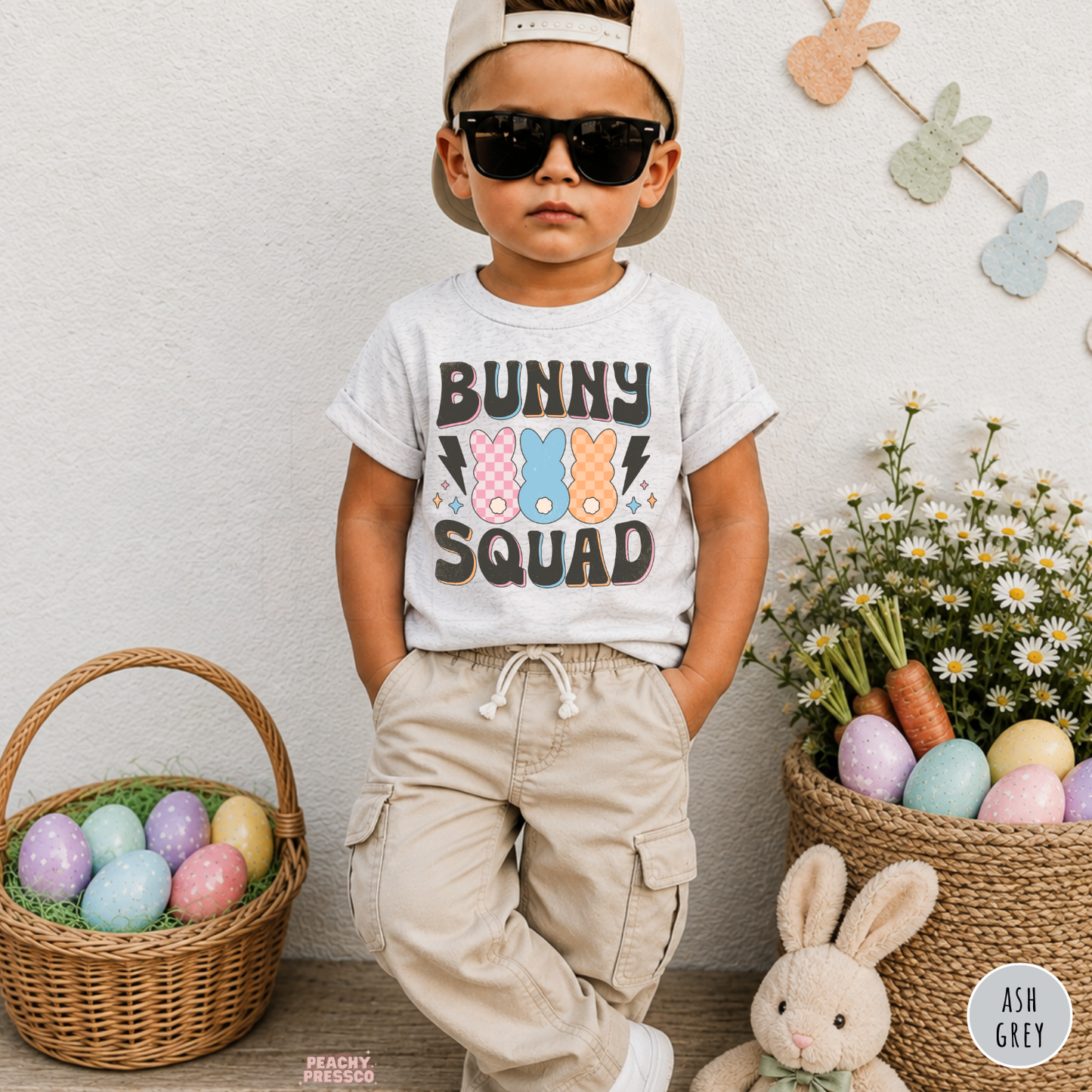 Toddler boy wearing an ash grey Bunny Squad Easter shirt with colorful retro bunny and pastel Easter decorations.