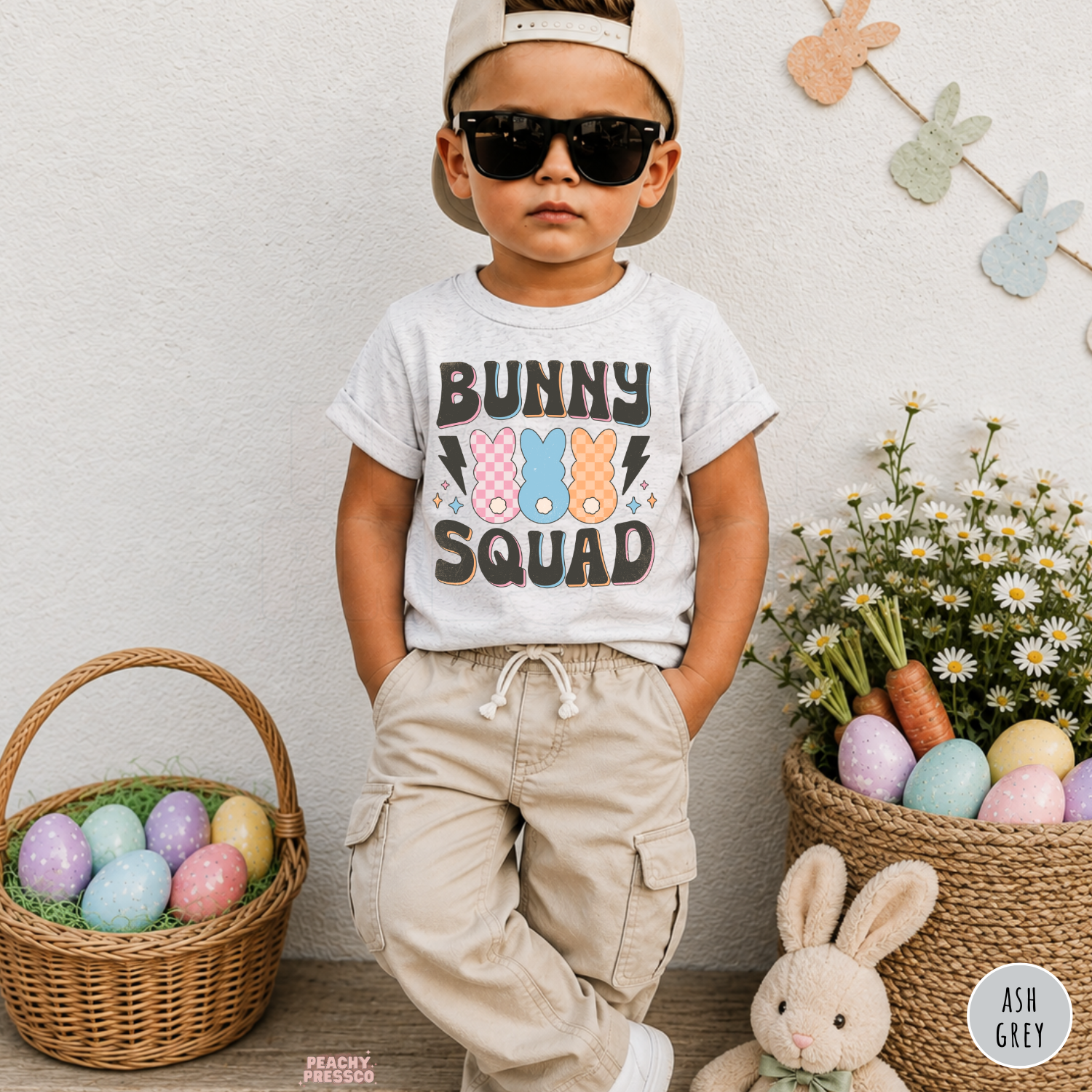 Toddler boy wearing an ash grey Bunny Squad Easter shirt with colorful retro bunny and pastel Easter decorations.