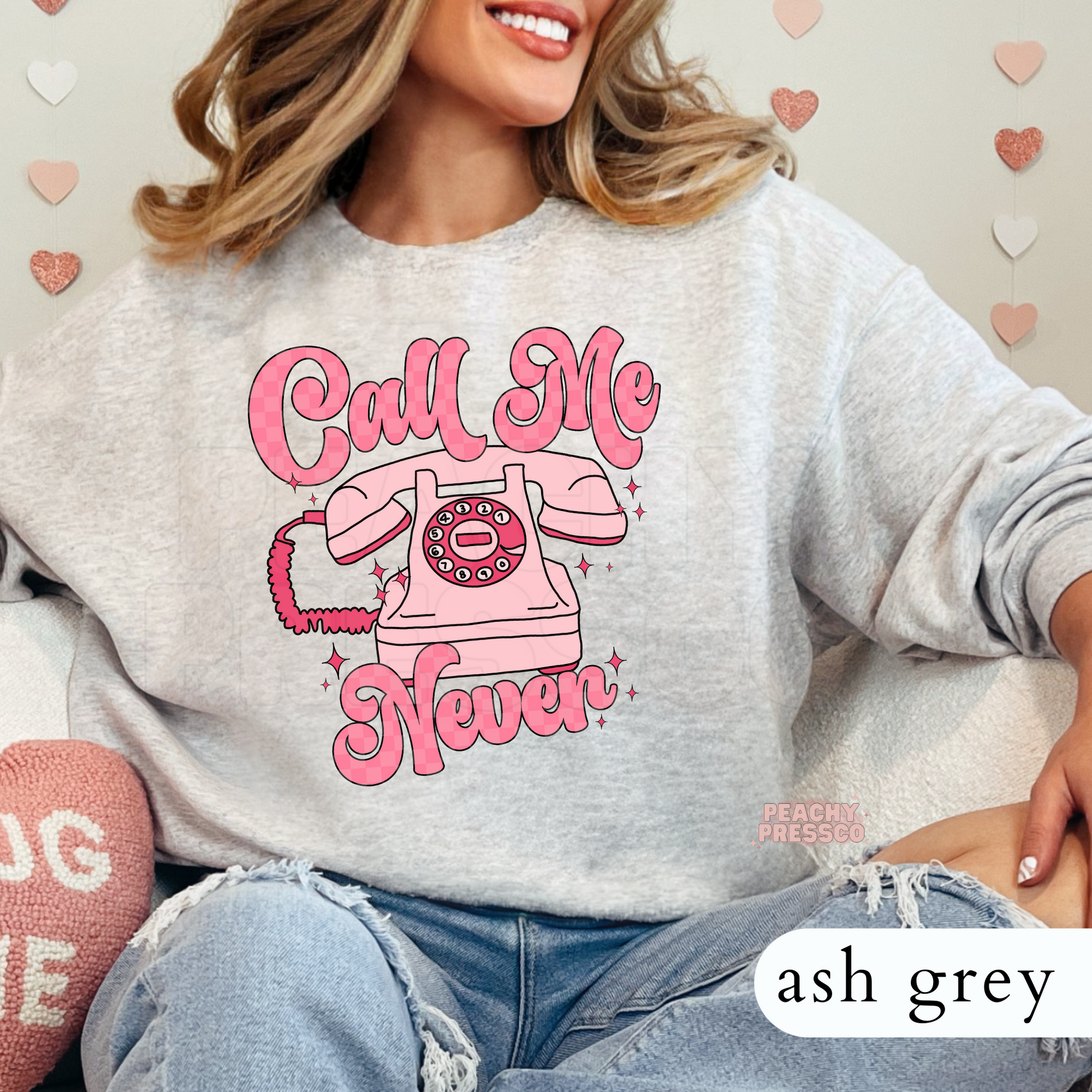 Call Me Never funny graphic on an ash grey crewneck sweatshirt featuring a vintage pink rotary phone and retro Valentine's style artwork.
