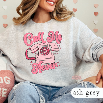 Call Me Never funny graphic on an ash grey crewneck sweatshirt featuring a vintage pink rotary phone and retro Valentine's style artwork.