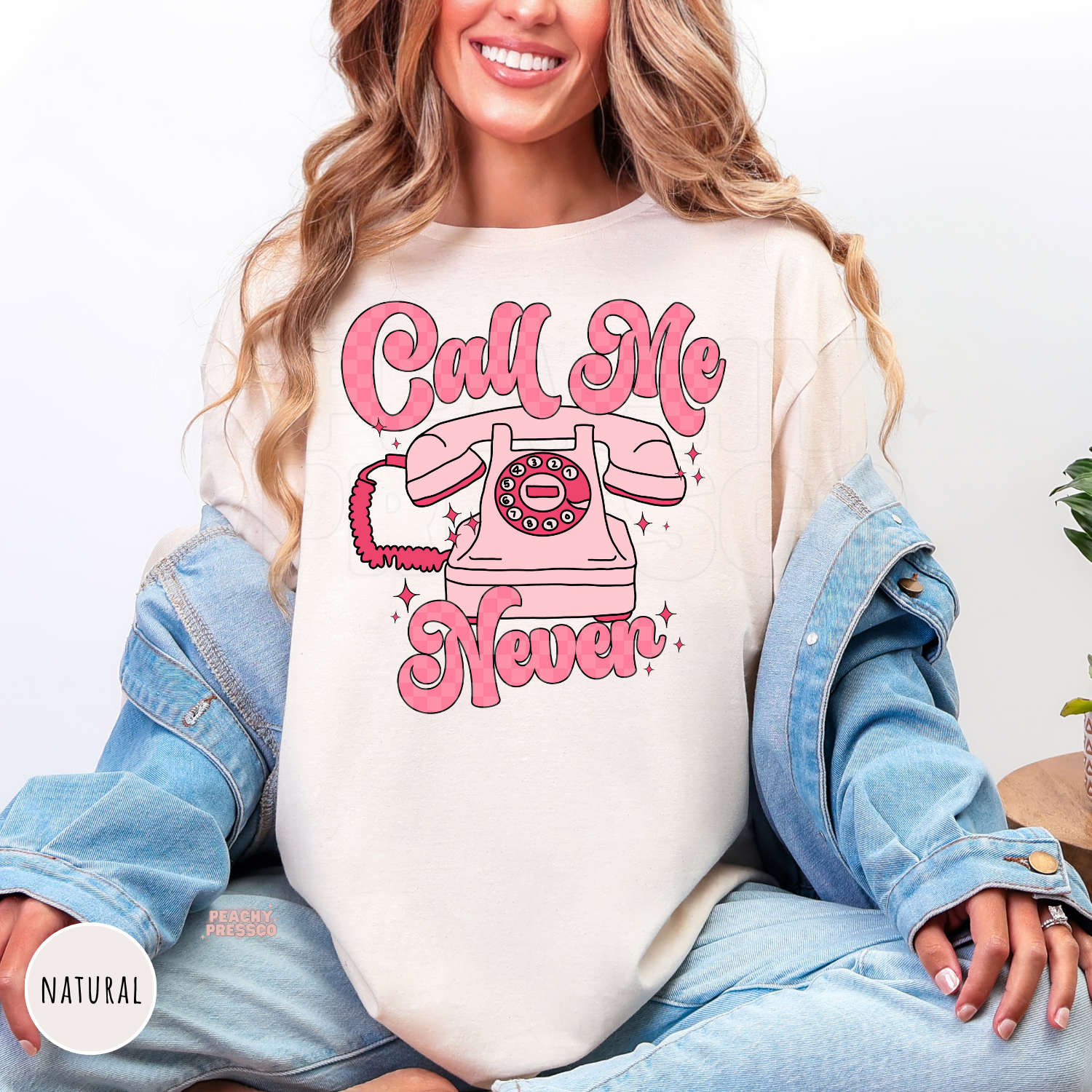 Funny Call Me Never graphic on a natural unisex t-shirt featuring a pink rotary telephone and retro Valentine's aesthetic.