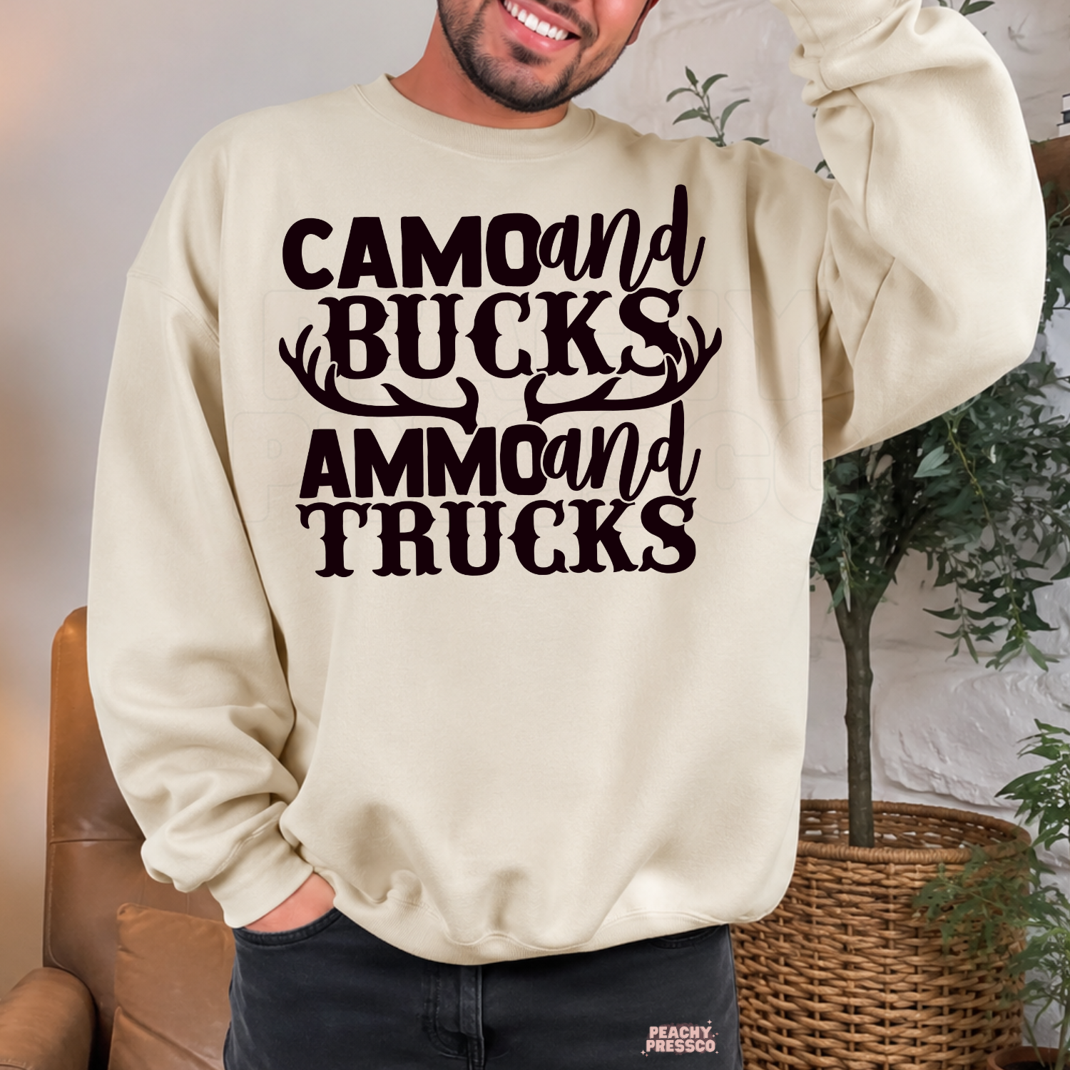 Sand crewneck sweatshirt featuring the "Camo and Bucks Ammo and Trucks" hunting graphic with antlers. Cozy gift for deer hunters, outdoorsmen, and country dads.