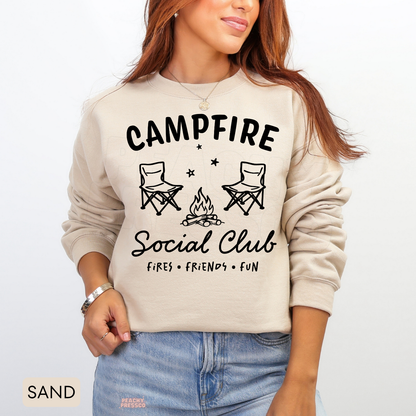 Sand Campfire Social Club sweatshirt with two camping chairs, a crackling campfire and fun camping-inspired typography.