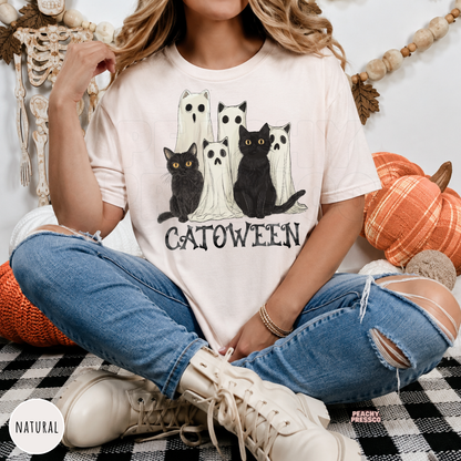 Woman wearing a natural Comfort Colors t-shirt with a Catoween design featuring adorable black cats and ghost costumes.