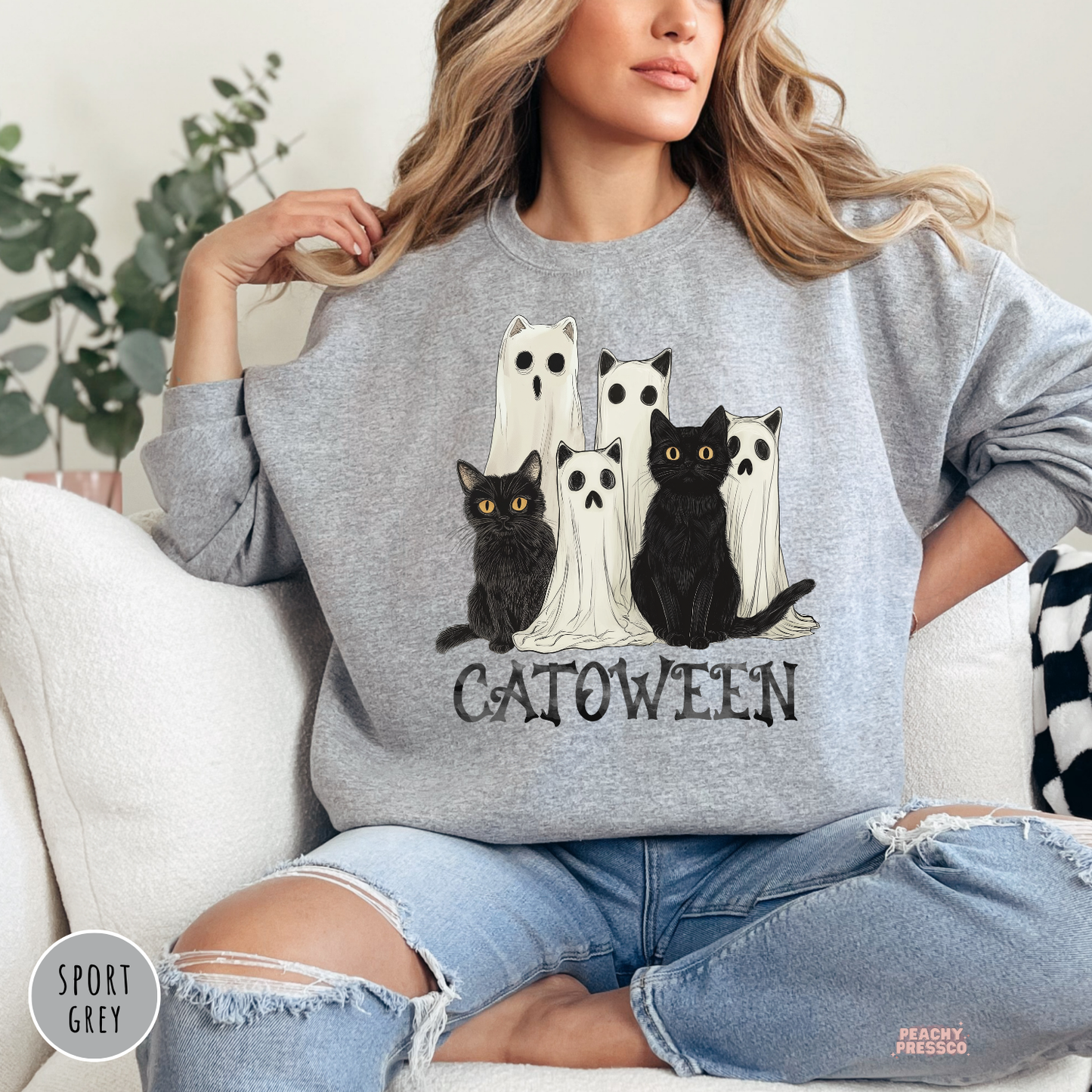 Woman wearing a sport grey crewneck sweatshirt with a Catoween graphic featuring black cats dressed as ghosts for Halloween.