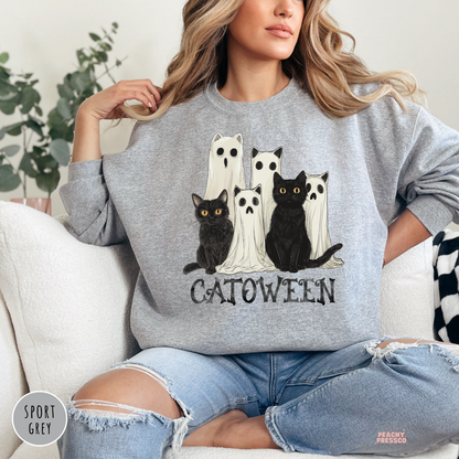 Woman wearing a sport grey crewneck sweatshirt with a Catoween graphic featuring black cats dressed as ghosts for Halloween.