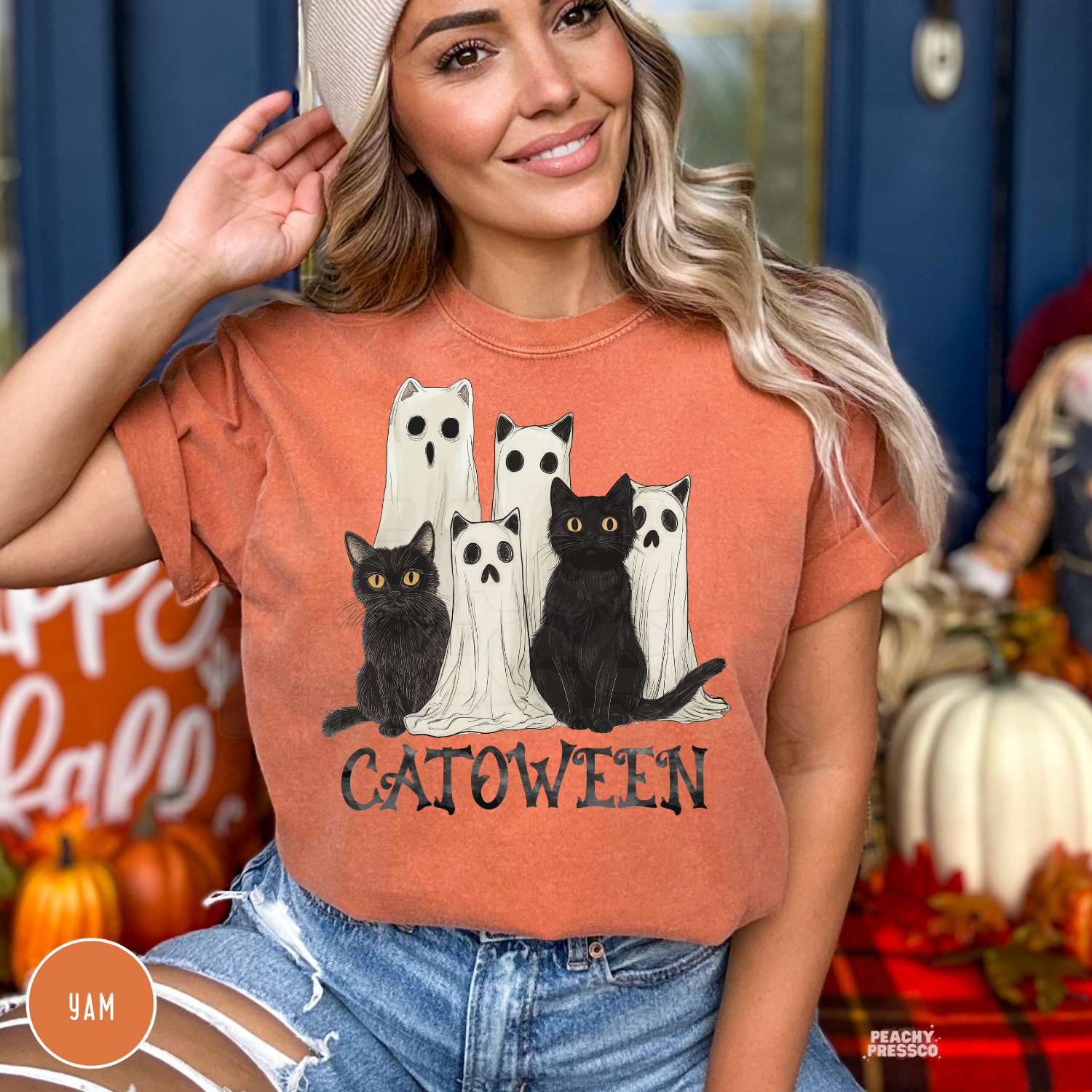 Woman wearing a Comfort Colors yam t-shirt featuring a Catoween graphic with black cats and ghost cats for spooky season.