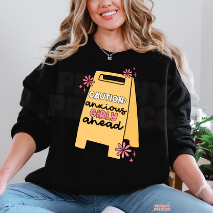 Black Caution Anxious Girly Ahead sweatshirt featuring a bright yellow warning sign, pink daisy illustrations and a funny anxiety-themed graphic.